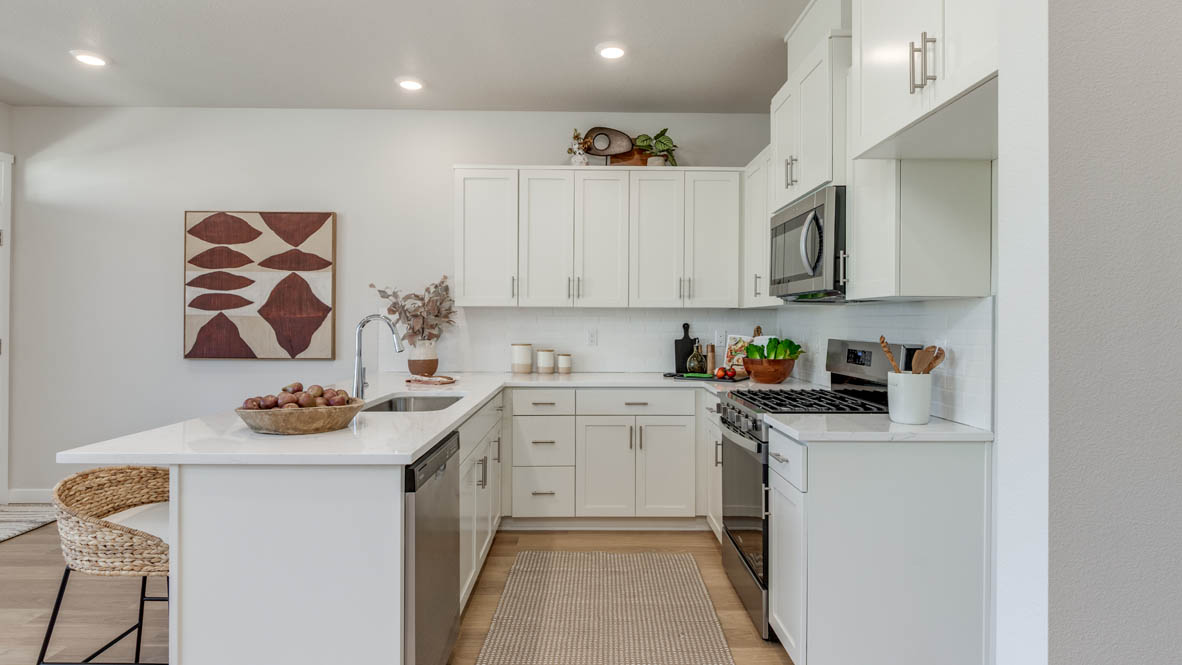 Gordon Creek Pointe Kitchen with stool chairs, quartz countertops, island peninsula, stainless steel appliances, white cabinets, laminate flooring, and decorative painting