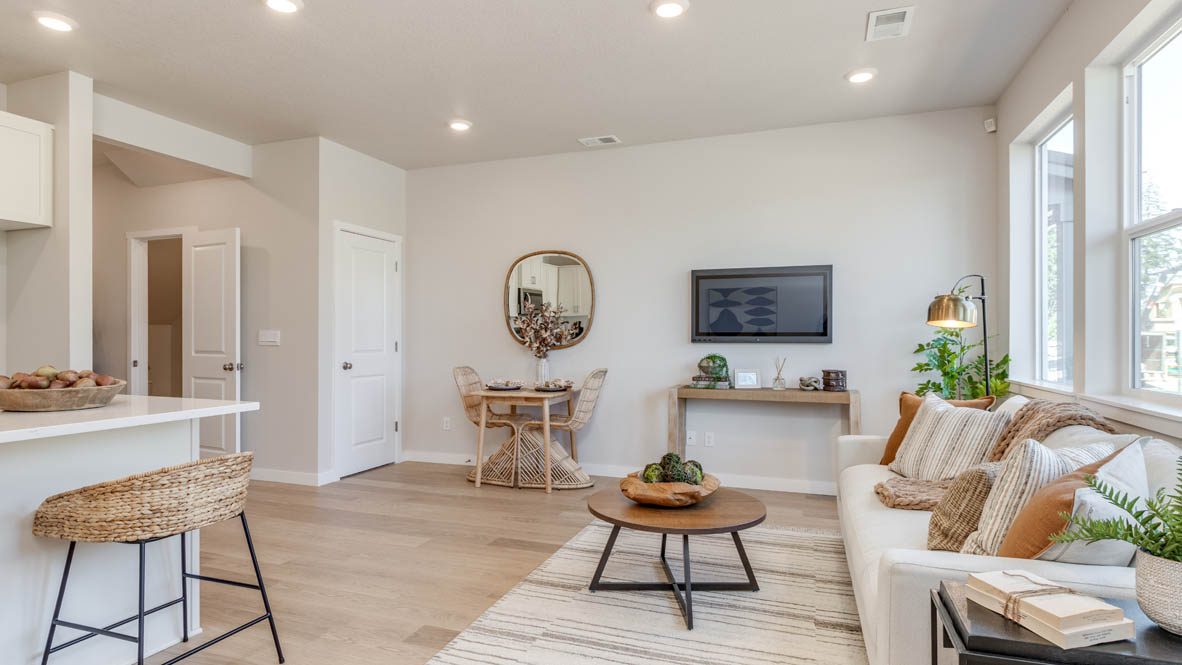 Gordon Creek Pointe Great Room with a coffee table, white couch with pillows, windows, a tv and entertainment center, a plant, with the dining table and circle mirror in the background