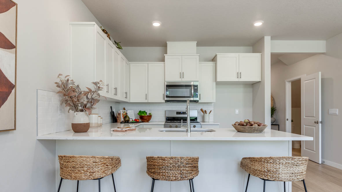 Gordon Creek Pointe Kitchen with stool chairs, quartz countertops, island peninsula, stainless steel appliances, white cabinets, laminate flooring, and decorative painting