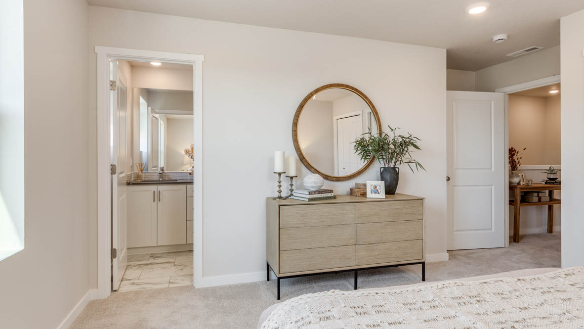 Gordon Creek Pointe Primary bedroom with carpet, dresser with plants, circle mirror, and the bathroom in the background