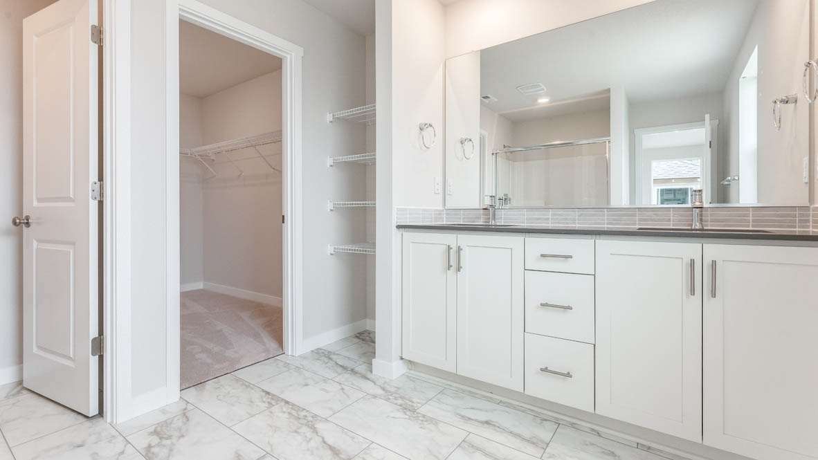 Gordon Creek Pointe primary bathroom with quartz countertops, white cabinets, mirror, and the walk in closet in the background