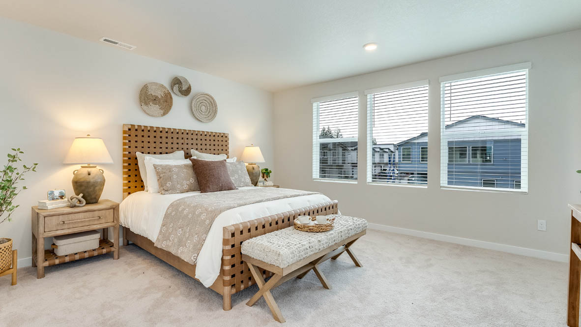 Gordon Creek Pointe primary bedroom with three windows, carpet, bed with two nightstands, comforter