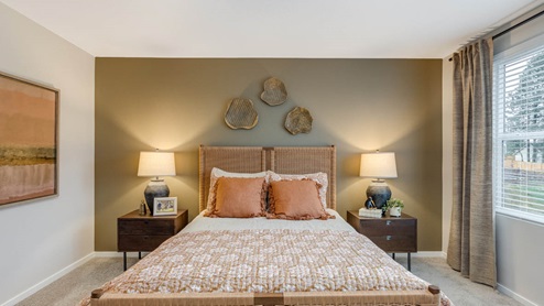 Blue Pearl Primary bedroom with accent wall, two windows with drapes, carpeting, and bed with peach colored bedding