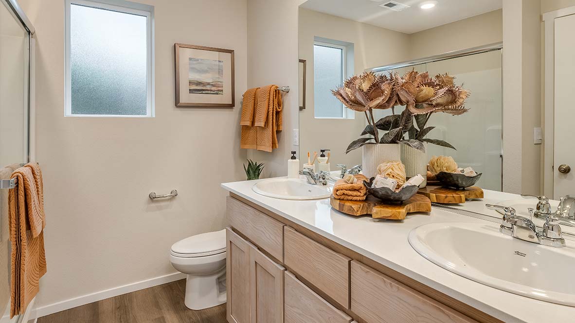 Blue Pearl Primary Bathroom with two sink vanity, walk in shower with glass sliding door, and light wood cabinets