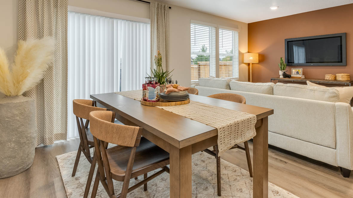 Blue Pearl great room with an L shaped couch, laminate flooring with an area rug, a coffee table and a media console connected to the dining room with 4 place settings