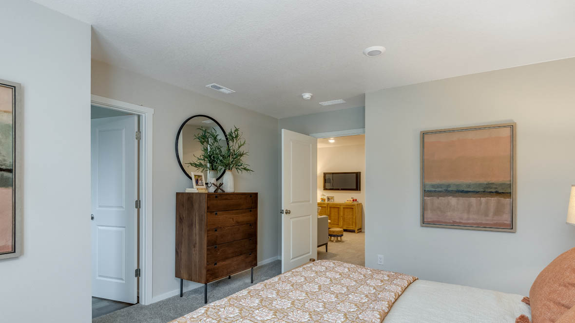 Blue Pearl Primary bedroom with accent wall, two windows with drapes, carpeting, and bed with peach colored bedding