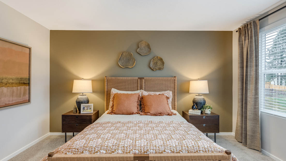 Blue Pearl Primary bedroom with accent wall, two windows with drapes, carpeting, and bed with peach colored bedding