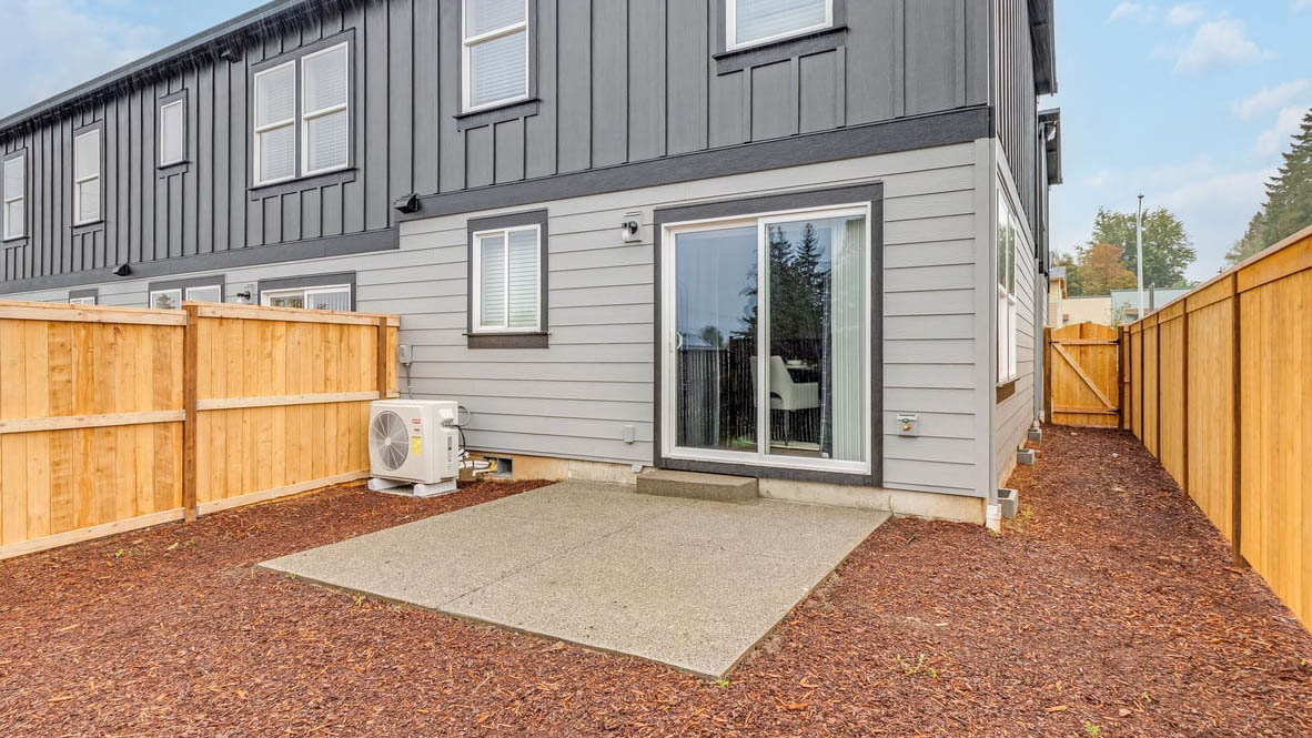 fully fenced backyard with bark chips and a patio