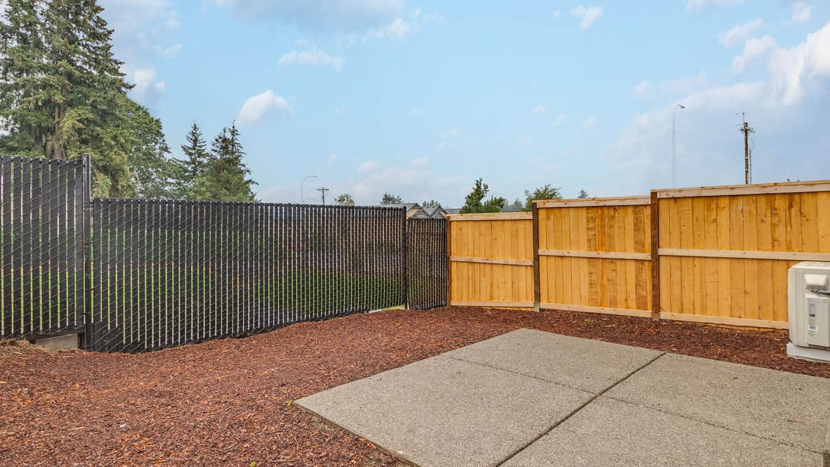 fully fenced backyard with bark chips and a patio