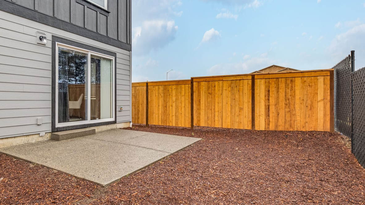 fully fenced backyard with bark chips and a patio