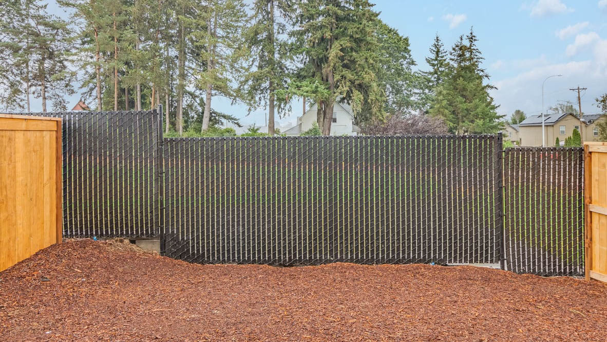 fully fenced backyard with bark chips and a patio