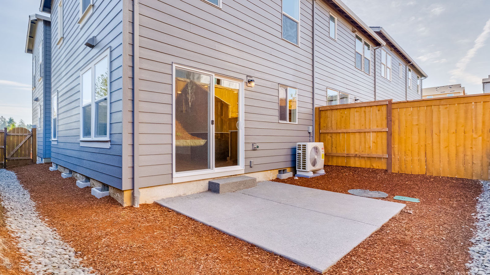 fully fenced backyard with bark chips and a patio