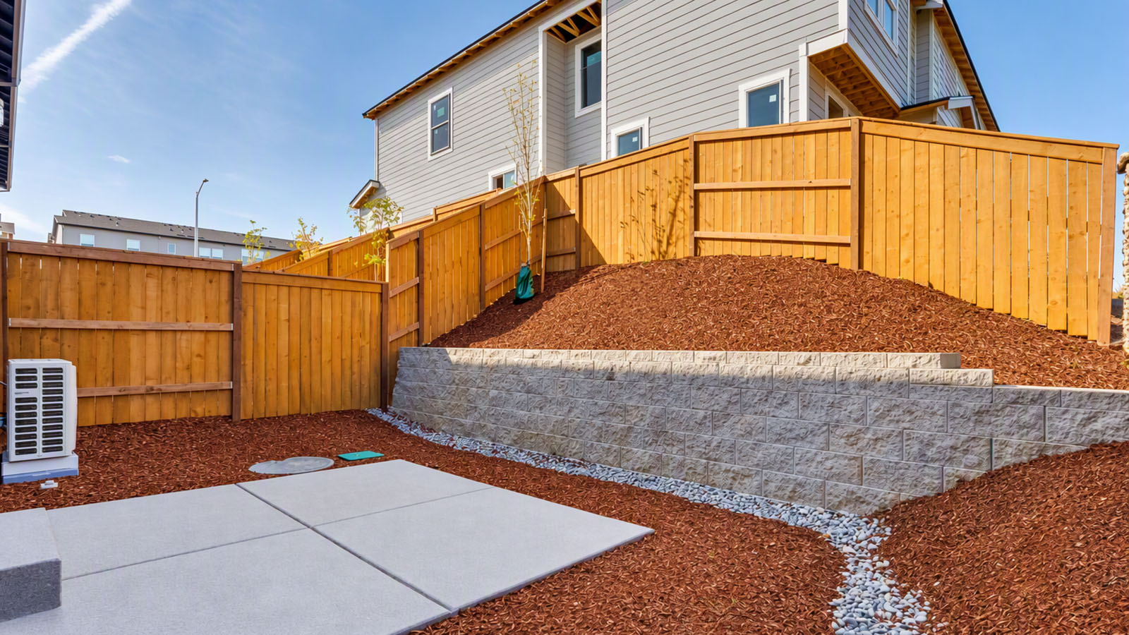 fully fenced backyard with bark chips and a patio