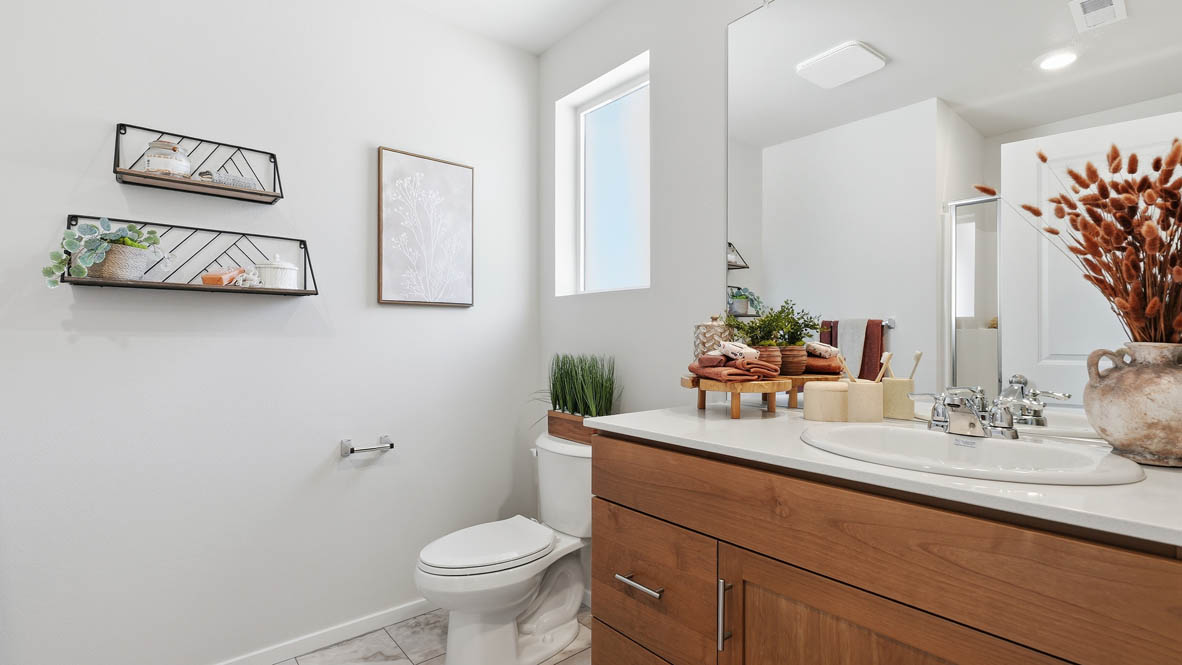 Thunder Ridge primary bathroom with stained shaker style cabinets with brushed nickel pulls under solid surface countertops and a walk in shower