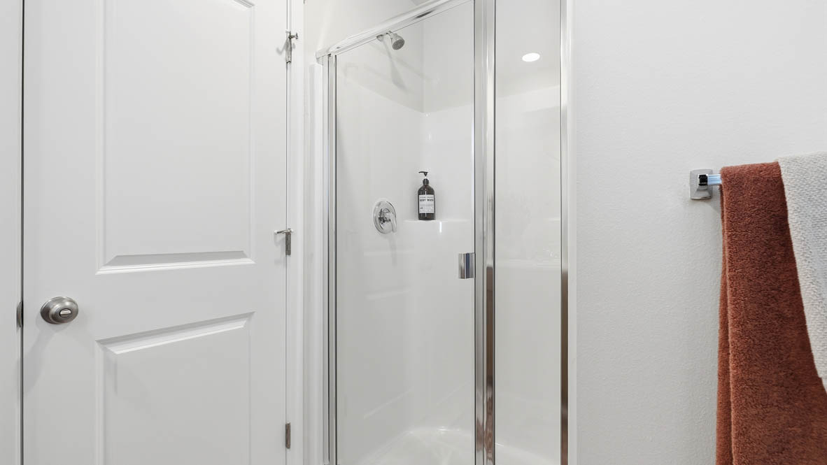 Thunder Ridge primary bathroom with stained shaker style cabinets with brushed nickel pulls under solid surface countertops and a walk in shower