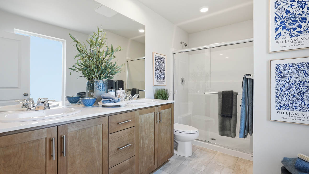 Thunder Ridge primary bathroom with stained shaker style cabinets with brushed nickel pulls under solid surface countertops and a walk in shower