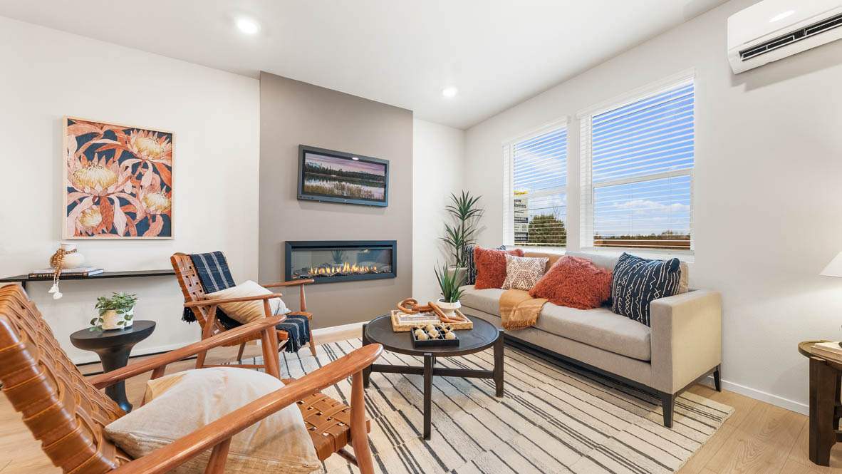 Ponderosa Great room with a white couch and pillows, electric fireplace, chair, white rug, wood coffee table, laminate flooring, a lamp, and windows
