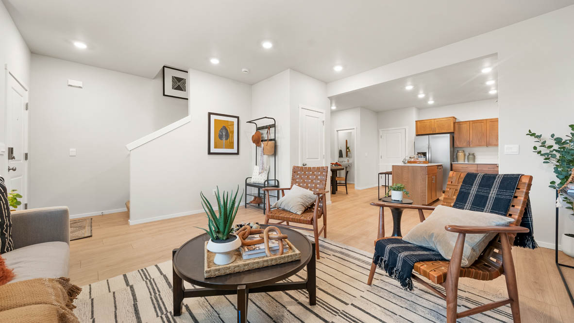 Ponderosa Great room with a white couch and pillows, chair, rug, wood coffee table, laminate flooring, a lamp, and kitchen in the background