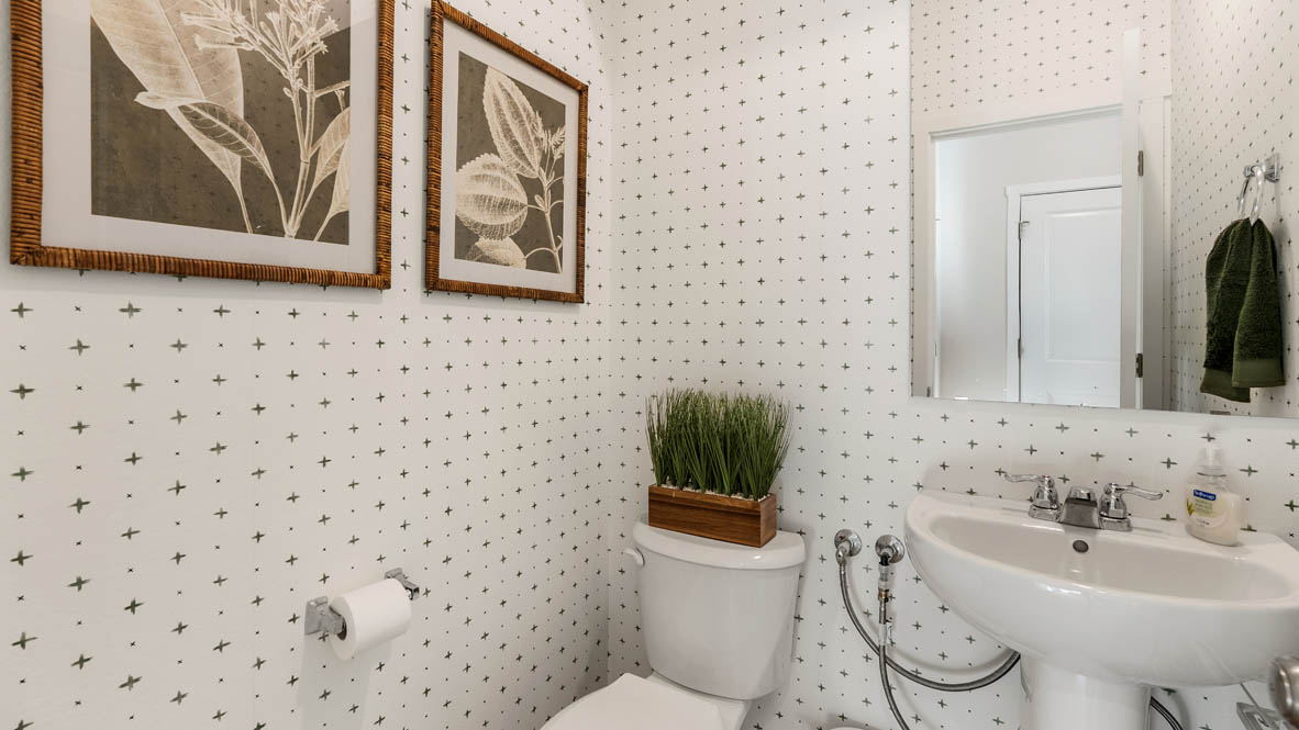 Ponderosa powder room with white single sink vanity, a round mirror, toilet with a grass plant, two paintings, and white walls