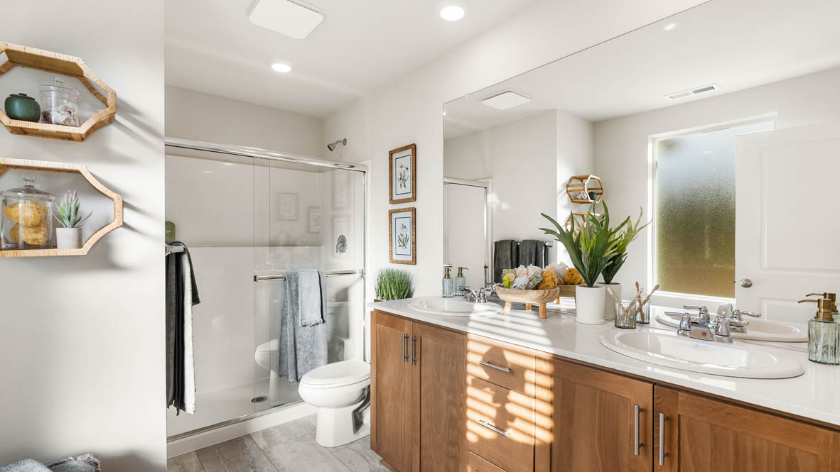 Ponderosa primary bathroom with stained shaker style cabinets with brushed nickel pulls under solid surface countertops and a walk in shower