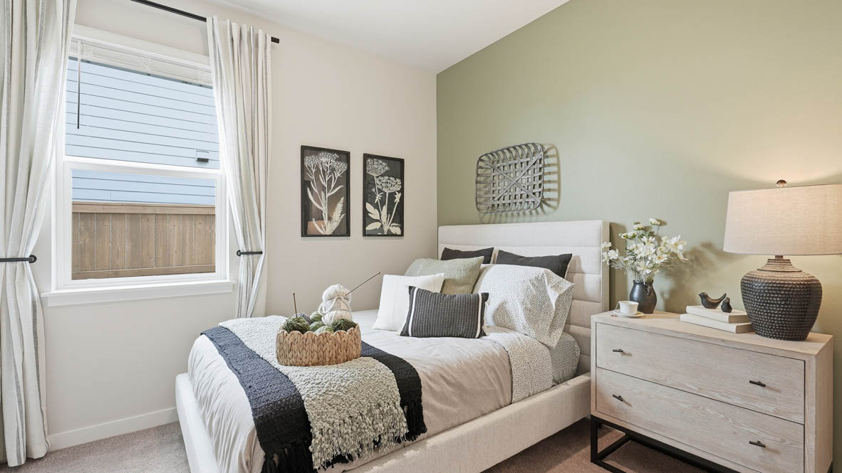 Stevens Ranch bedroom on the main floor with light green accent wall and bed with dresser to the right hand side