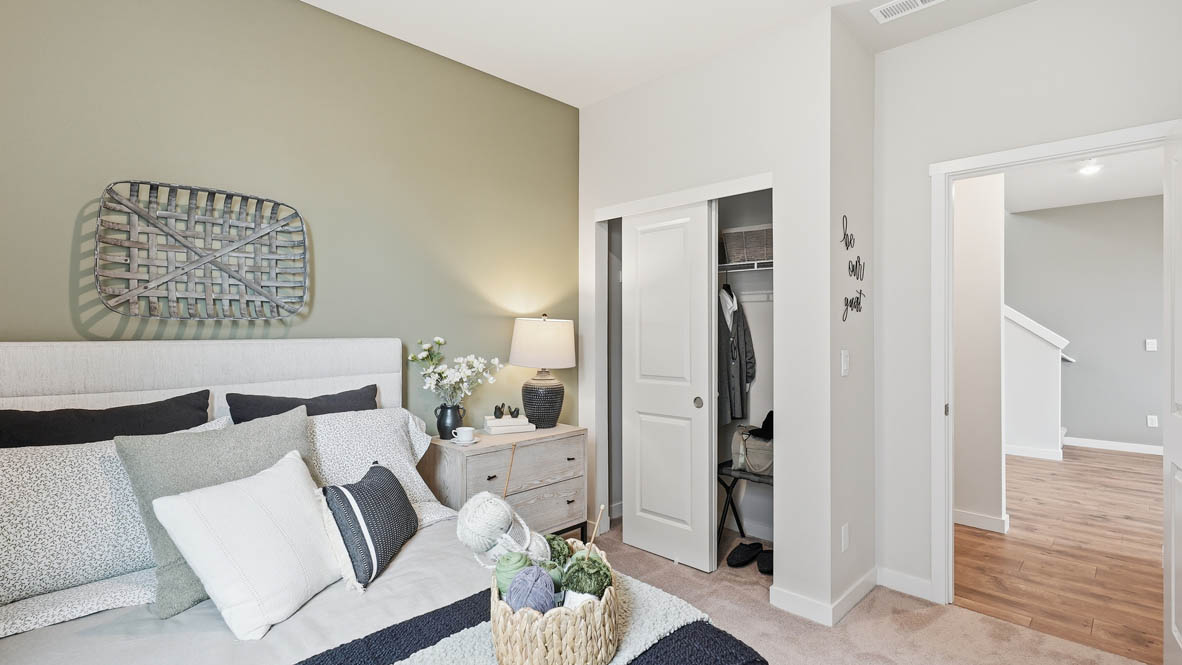 Stevens Ranch bedroom on the main floor with light green accent wall and bed with dresser to the right hand side