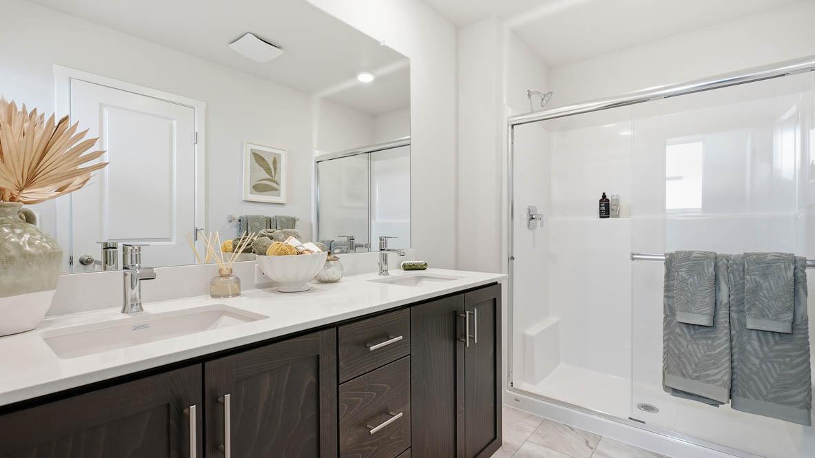 Stevens Ranch primary bathroom with dark stained shaker style cabinets on a double sink vanity with white quartz countertops and walk in standing shower