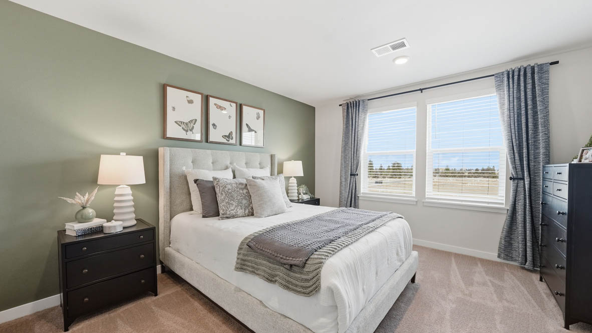 Stevens Ranch bedroom with carpet flooring and windows, bed with green accent blanket and pillows, two paintings, two nightstands, two lamps