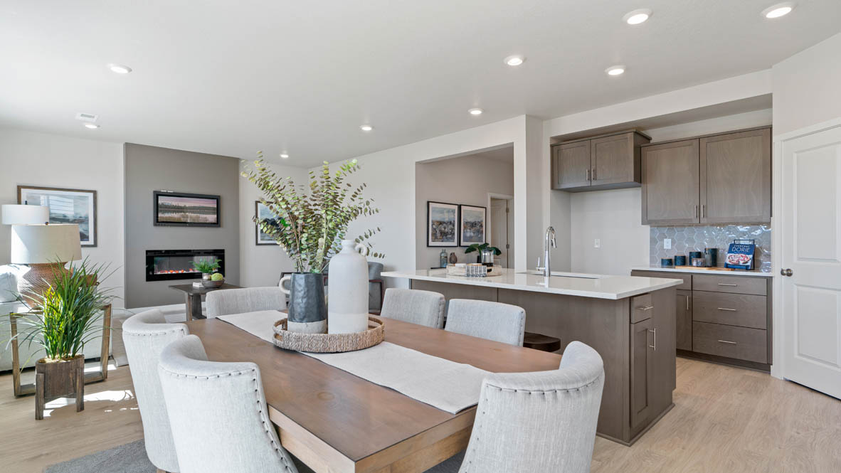 Stevens Ranch dining room with table, four chairs, windows, painting, laminate flooring, with the kitchen in the background.