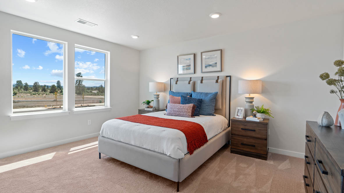 Stevens Ranch primary bedroom with carpet, two windows, paintings, bed with red blanket, nightstands with lamps, and dresser