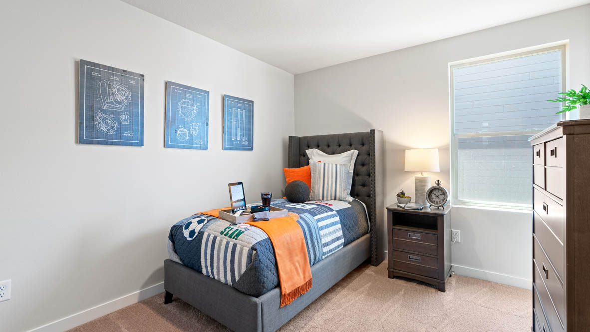 Stevens Ranch bedroom with blue blankets and orange blanket, nightstand with lamp, dresser, and paintings