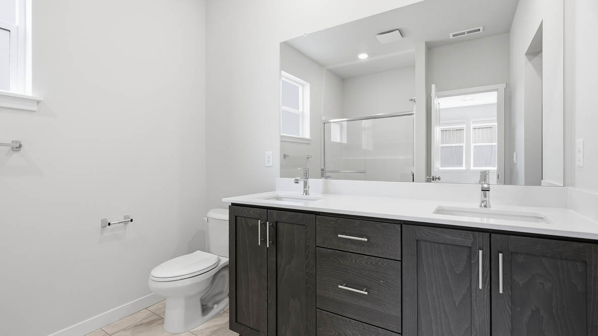 Stevens Ranch primary bathroom with double sink vanity, mirror, brown stained cabinets, and toilet
