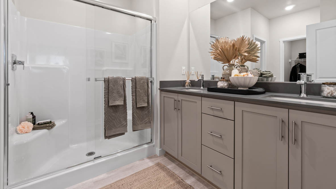 Stevens Ranch primary bathroom with laminate flooring, grey cabinets, quartz countertops, double vanity, walk-in shower with sliding glass door