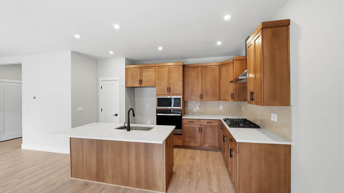Stevens Ranch kitchen with wood cabinets, backsplash, solid surface countertops, island, and stainless steel appliances