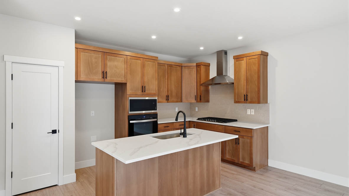Stevens Ranch kitchen with wood cabinets, backsplash, solid surface countertops, island, and stainless steel appliances