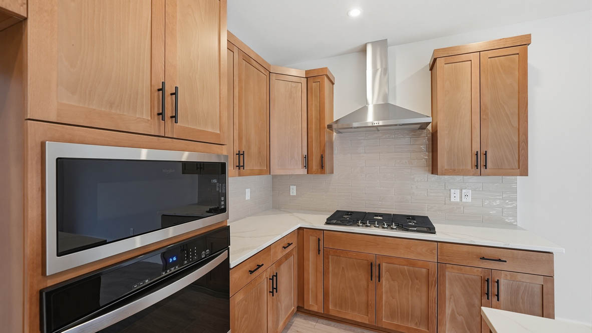 Stevens Ranch kitchen with wood cabinets, backsplash, solid surface countertops, island, and stainless steel appliances