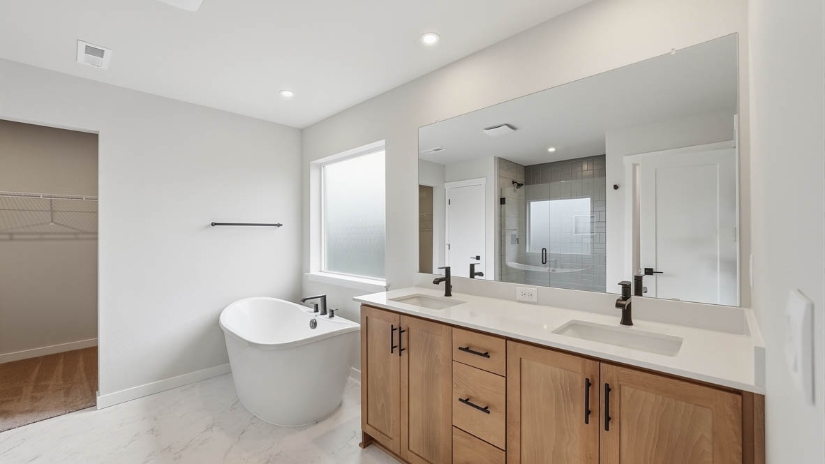 Stevens Ranch primary bathroom with double sink vanity, mirror, solo standing tub, window, and white walls