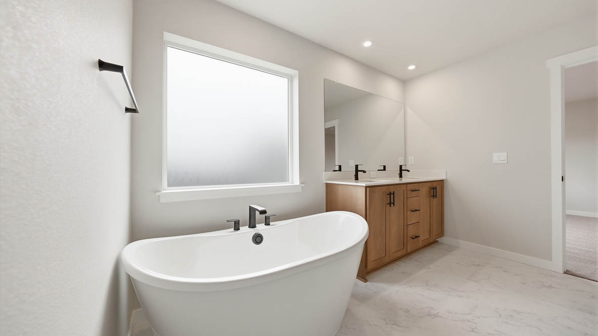 Stevens Ranch primary bathroom with double sink vanity, mirror, solo standing tub, window, and white walls