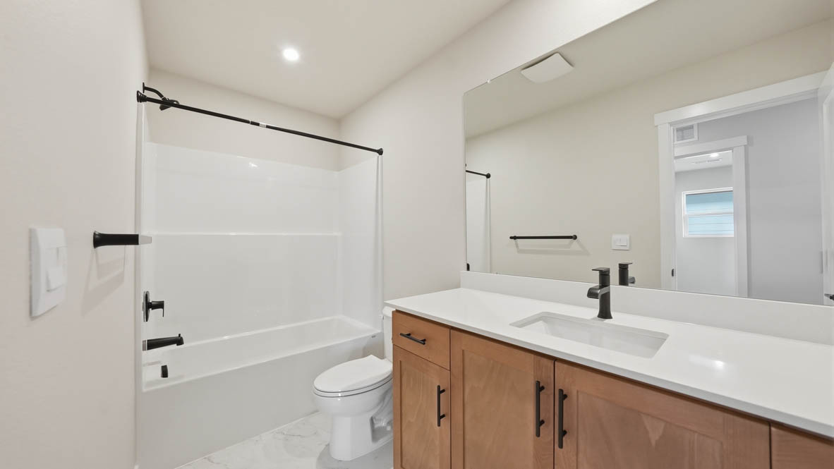 Stevens Ranch bathroom with wood cabinets, vanity, mirror, toilet, and tub shower