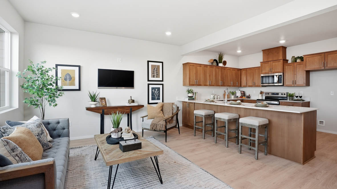 Stevens Ranch Townhomes great room and kitchen with a coffee table, a credenza, chair, tv, two paintings, three stools, and the kitchen in the background