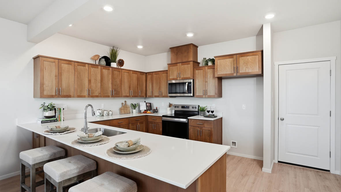 Stevens Ranch Townhomes kitchen with stained soft-closed cabinets, solid surface countertops, decorative plate sets, three stools, stainless steel appliances, laminate flooring, and white walls