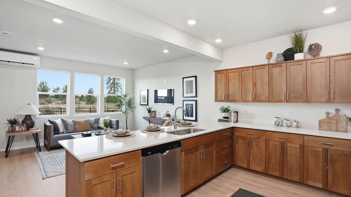 Stevens Ranch Townhomes kitchen with stained soft-closed cabinets, solid surface countertops, decorative plate sets, three stools, stainless steel appliances, laminate flooring, and the great room in the background