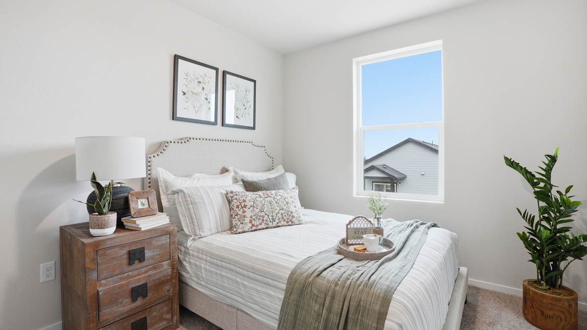 Stevens Ranch Townhomes bedroom with a rustic nightstand, lamp, plant, window, white walls, white comforter and bedding, and green accent blanket