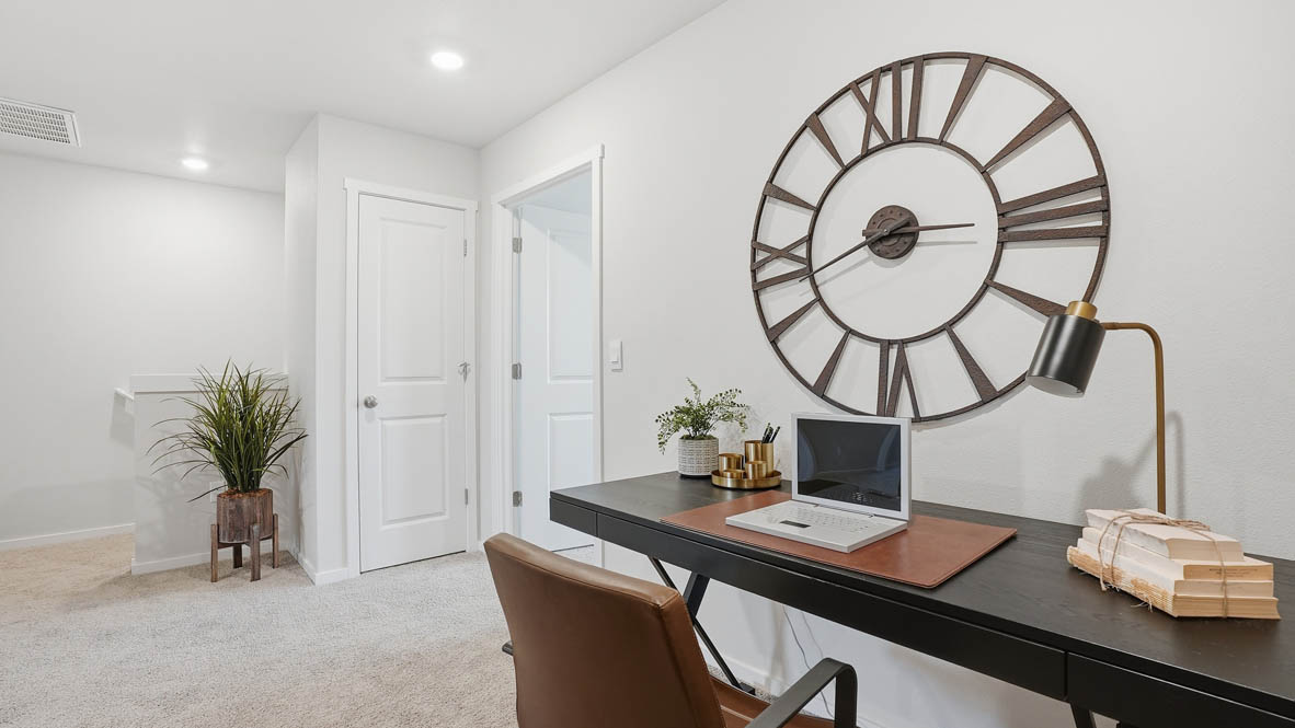 Stevens Ranch Townhomes loft with brass metal clock, black desk with a tiny lamp and books, laptop, brown chair, decorative plants, carpeting, white walls
