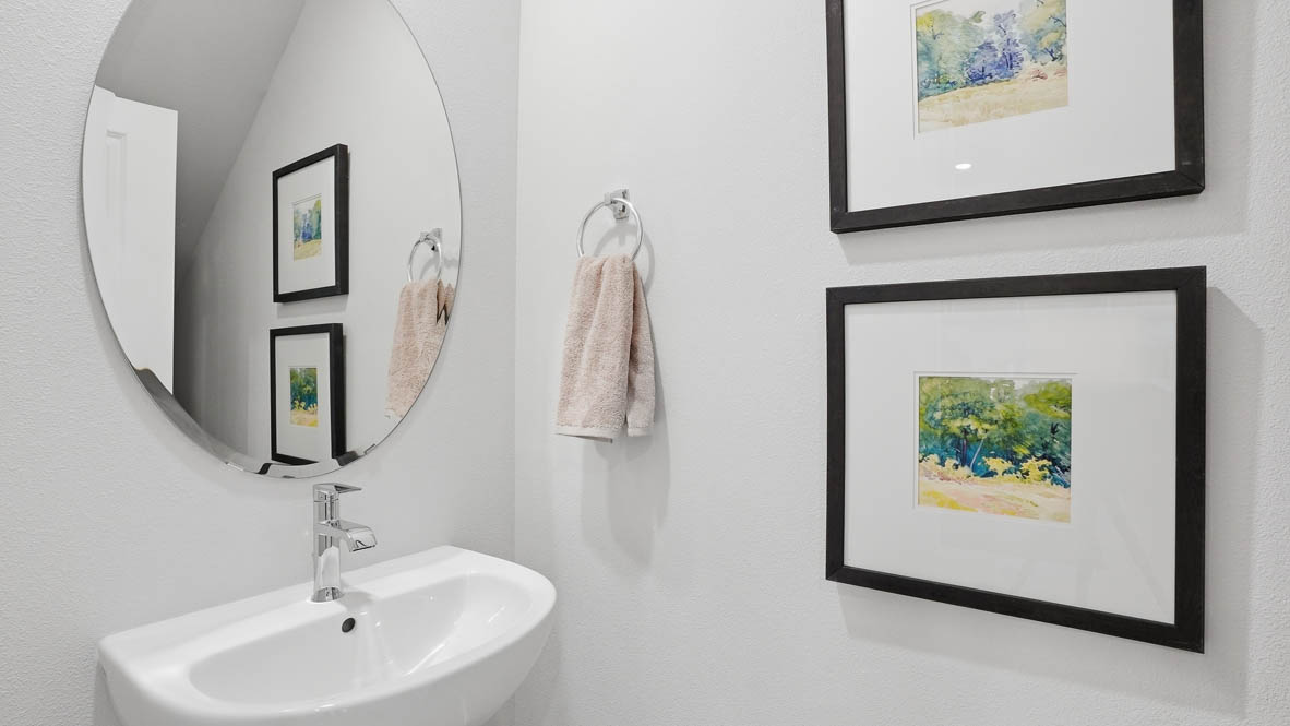 Stevens Ranch Townhomes powder bathroom with single sink vanity, oval mirror, two paintings, and one towel