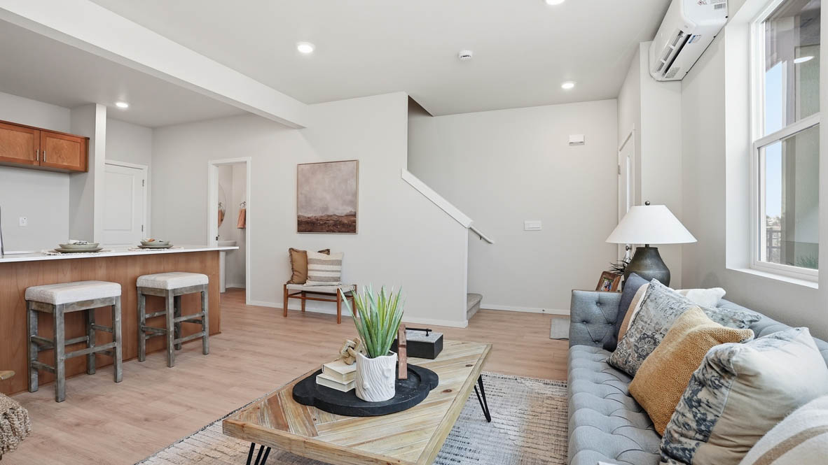 Stevens Ranch Townhomes great room with a wooden coffee table, wooden side table, lamp, gray couch, windows, tv, credenza, chair, three paintings, decorative plants, and a rug