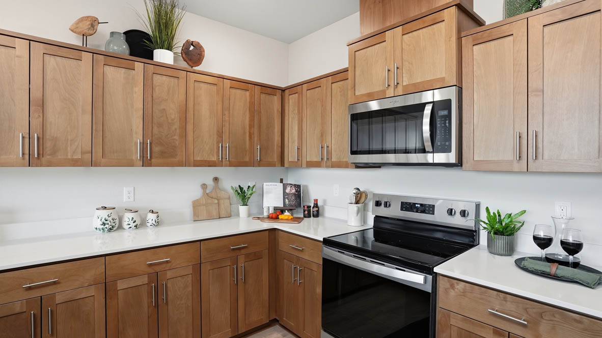 Stevens Ranch Townhomes kitchen with stained soft-closed cabinets, solid surface countertops, decorative plate sets, three stools, stainless steel appliances, laminate flooring, and white walls