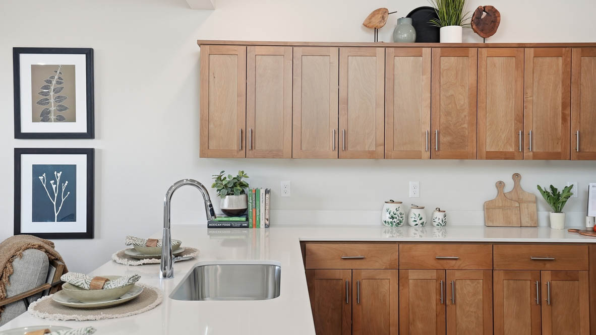 Stevens Ranch Townhomes kitchen with stained soft-closed cabinets, solid surface countertops, decorative plate sets, three stools, stainless steel appliances, laminate flooring, and white walls