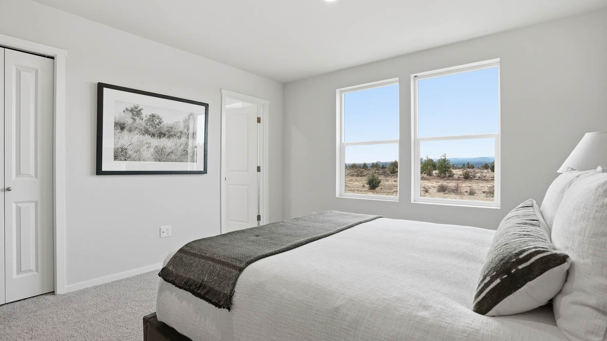 Stevens Ranch Townhomes primary bedroom with two windows, carpeting, white walls, olive bedding with white sheets, black nightstands, two lamps, circle mirror, and a dresser