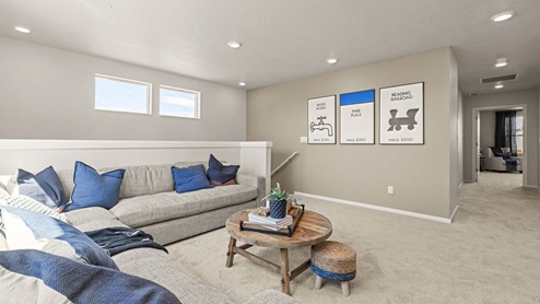 Monrovia carpeted Loft space with L shaped sectional couch, circular wooden coffee table with two small stools, a wall with board game themed art, and the hallway to more of the upstairs